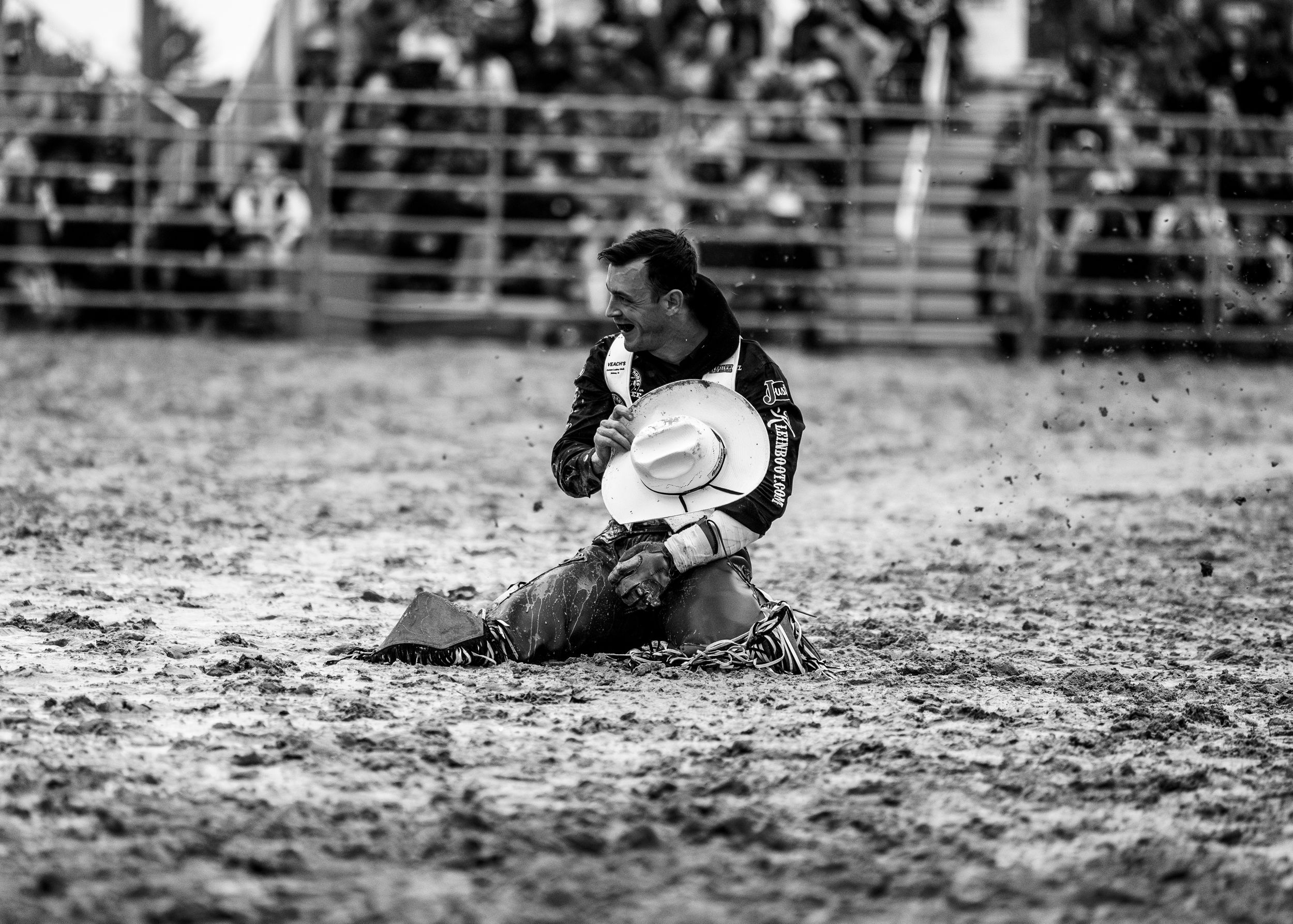 A black and white photo of a cowboy kneeling in the muddy rodeo arena, holding his hat to his chest after a ride.