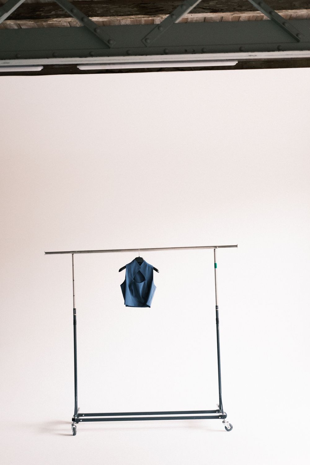 A minimalist clothing rack made of metal pipe mounted on a white wall displays a single blue garment.