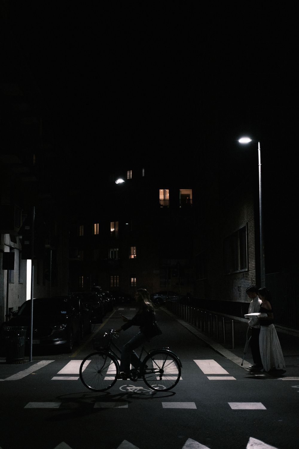A sequence of dark nighttime photos showing a bicycle crossing a zebra crossing illuminated by street lights.