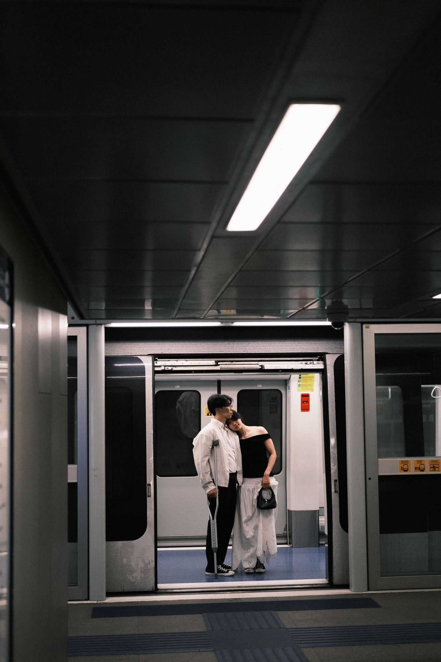 Two people standing between parallel escalators in a modern minimalist subway station with fluorescent lighting.