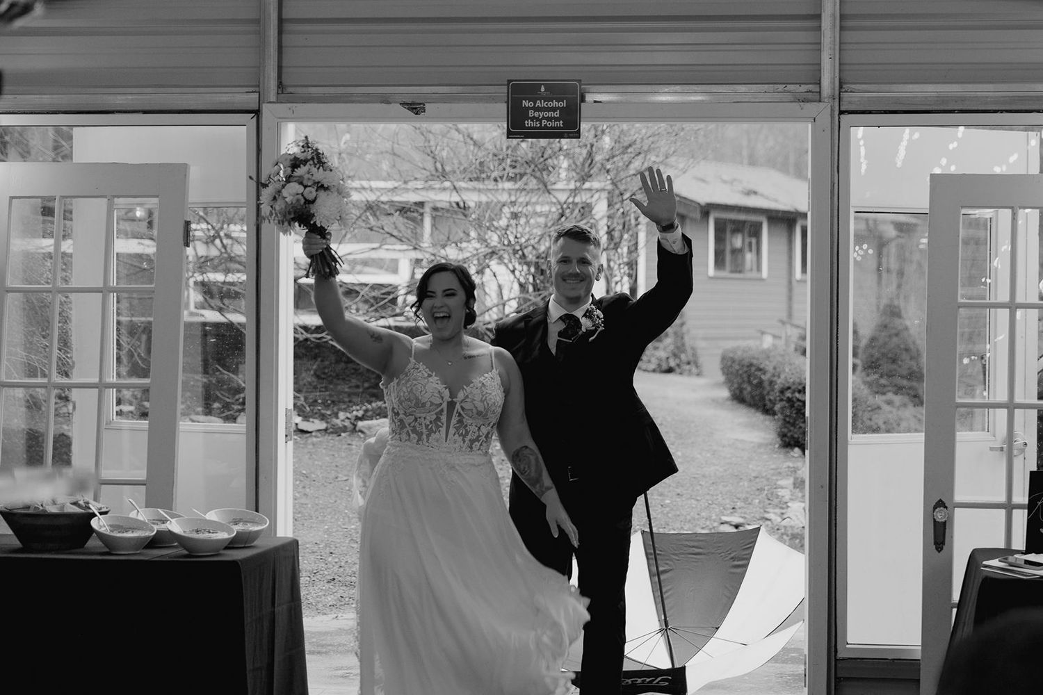 Black and white photo of newlyweds celebrating grand entrance through French doors at reception.