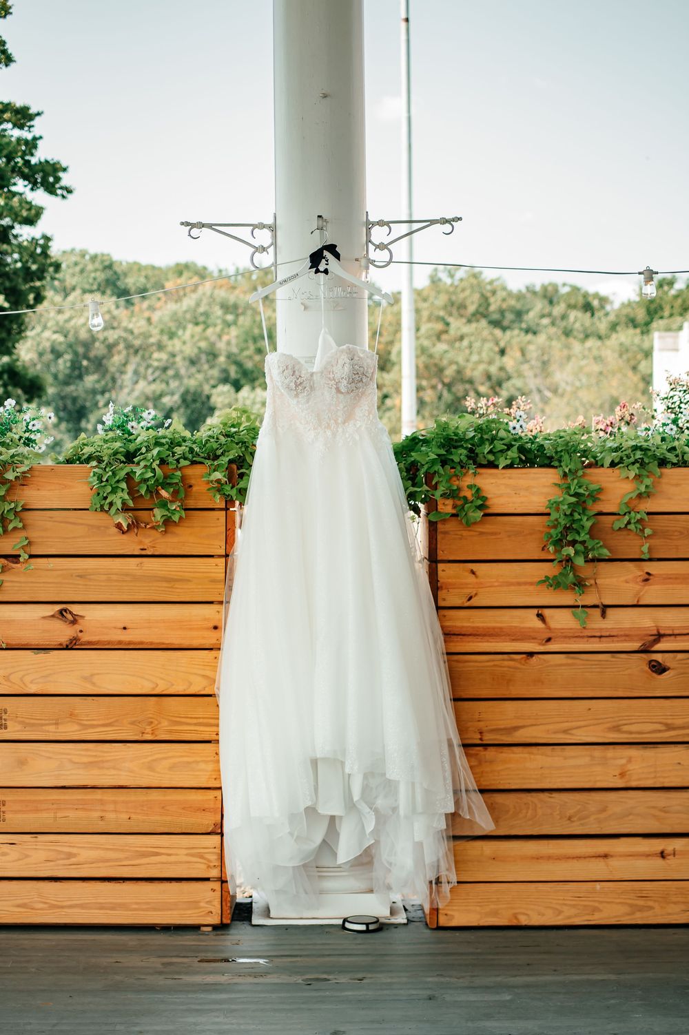 White wedding dress hanging against wooden planks with greenery decorations.