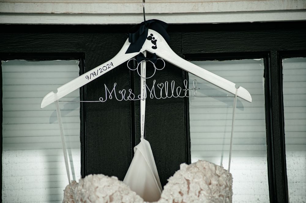Wedding dress displayed on a hanger with lace details against a white wall.