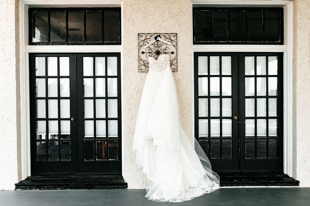 Row of elegant windows with ornate details frame a white wedding dress display.