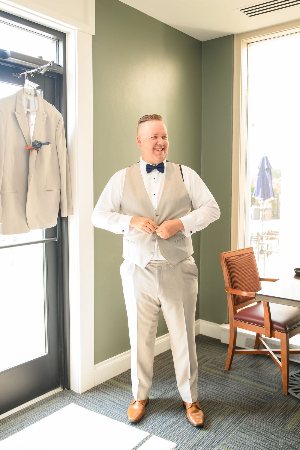Someone wearing a light colored formal suit adjusts their attire in a well-lit dressing room.
