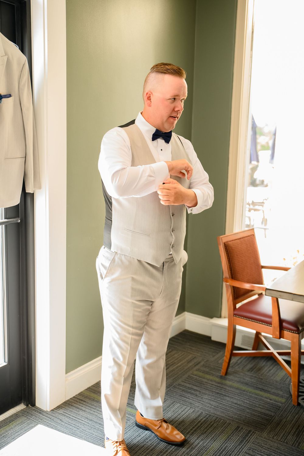 Person in white formal attire makes final adjustments in a dressing room with green walls.