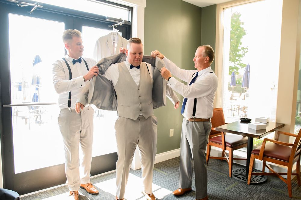Groomsmen in light gray suits and white shirts getting ready in a bright room with green walls.