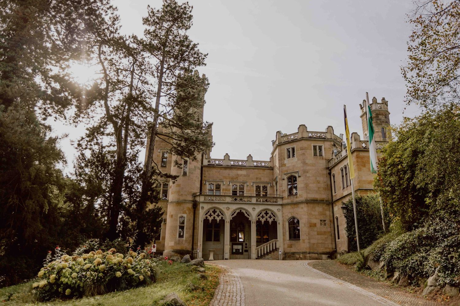 Gothic revival mansion with ornate stone architecture and arched entrance surrounded by trees and landscaping.