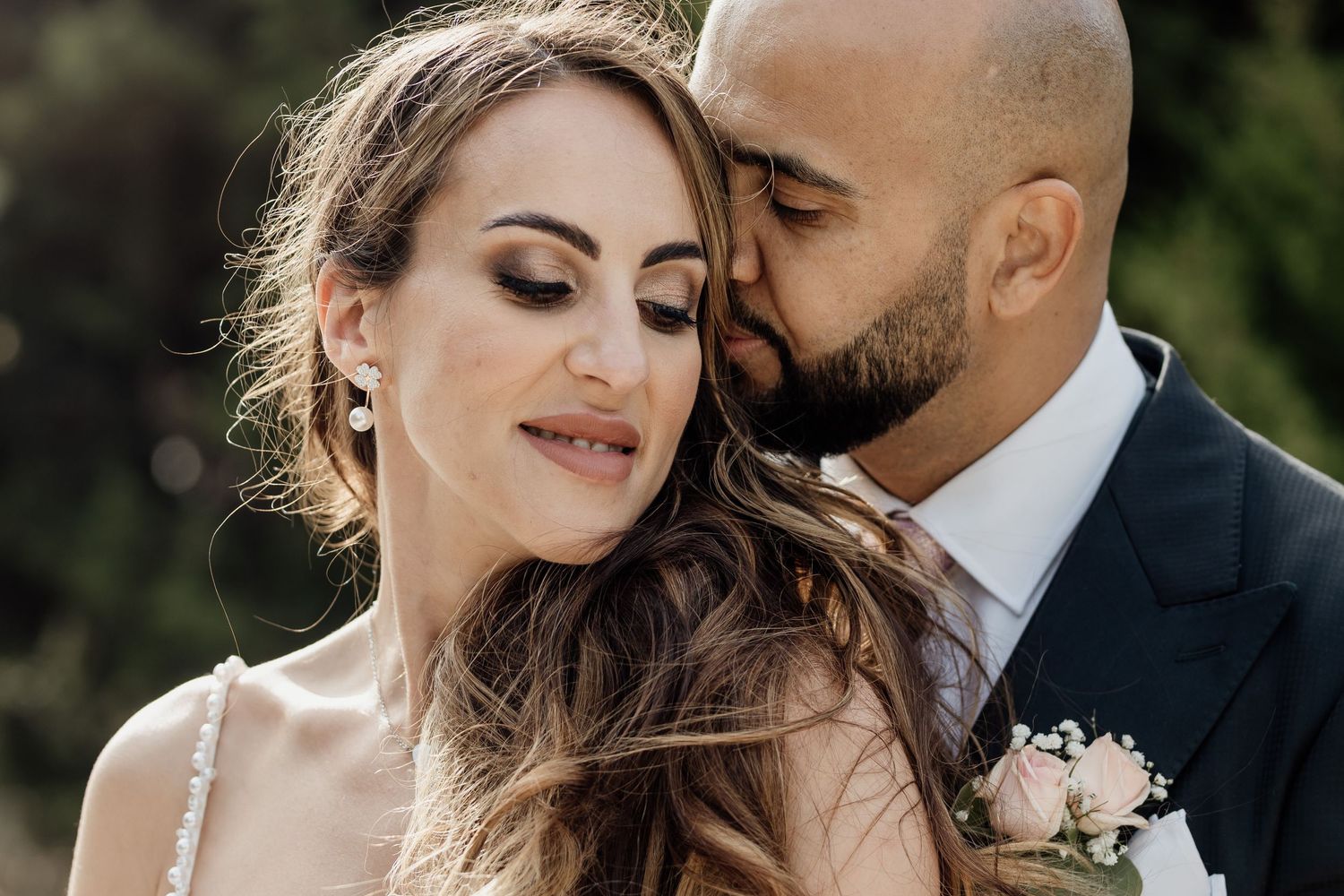 Close up romantic wedding portrait of bride and groom embracing outdoors with soft natural lighting.