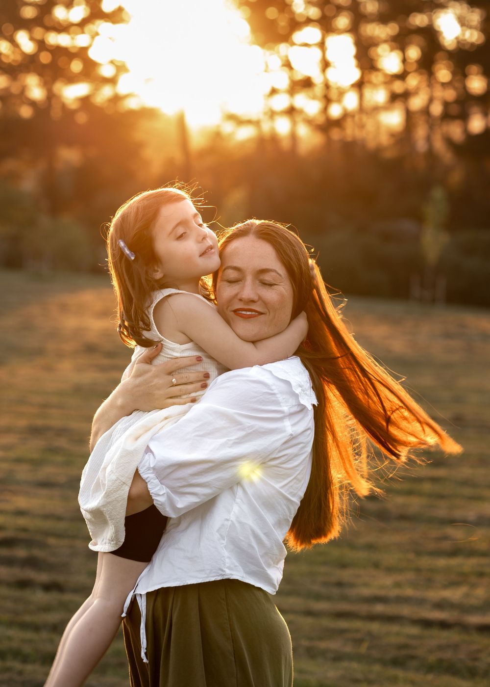 Mother clutching her young daughter swinging around in the sunset with trees in the background