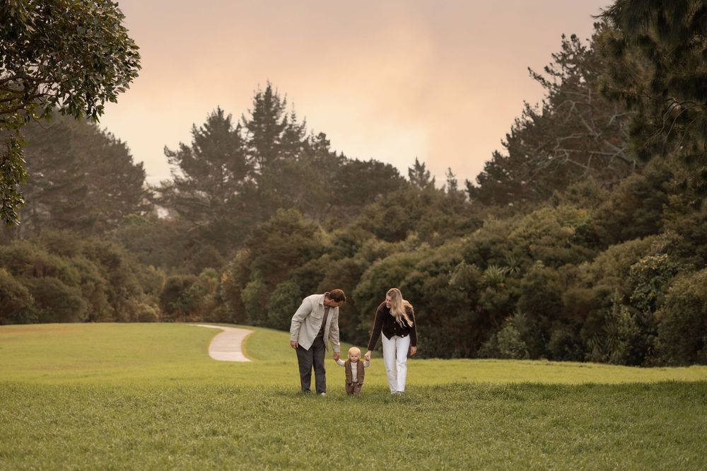 Sunset over trees and field with the mother and father holding hands with their toddler walking in a line. Family Sunset Photoshoot