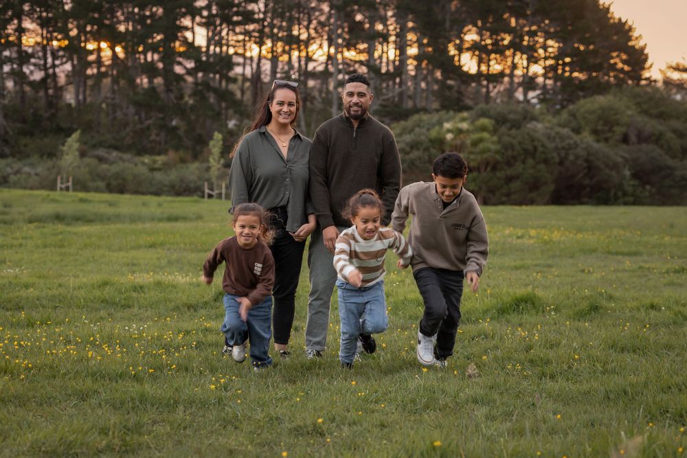 A fun family photo of parents standing smiling at the camera while the 3 children run towards the camera with smiles beaming
