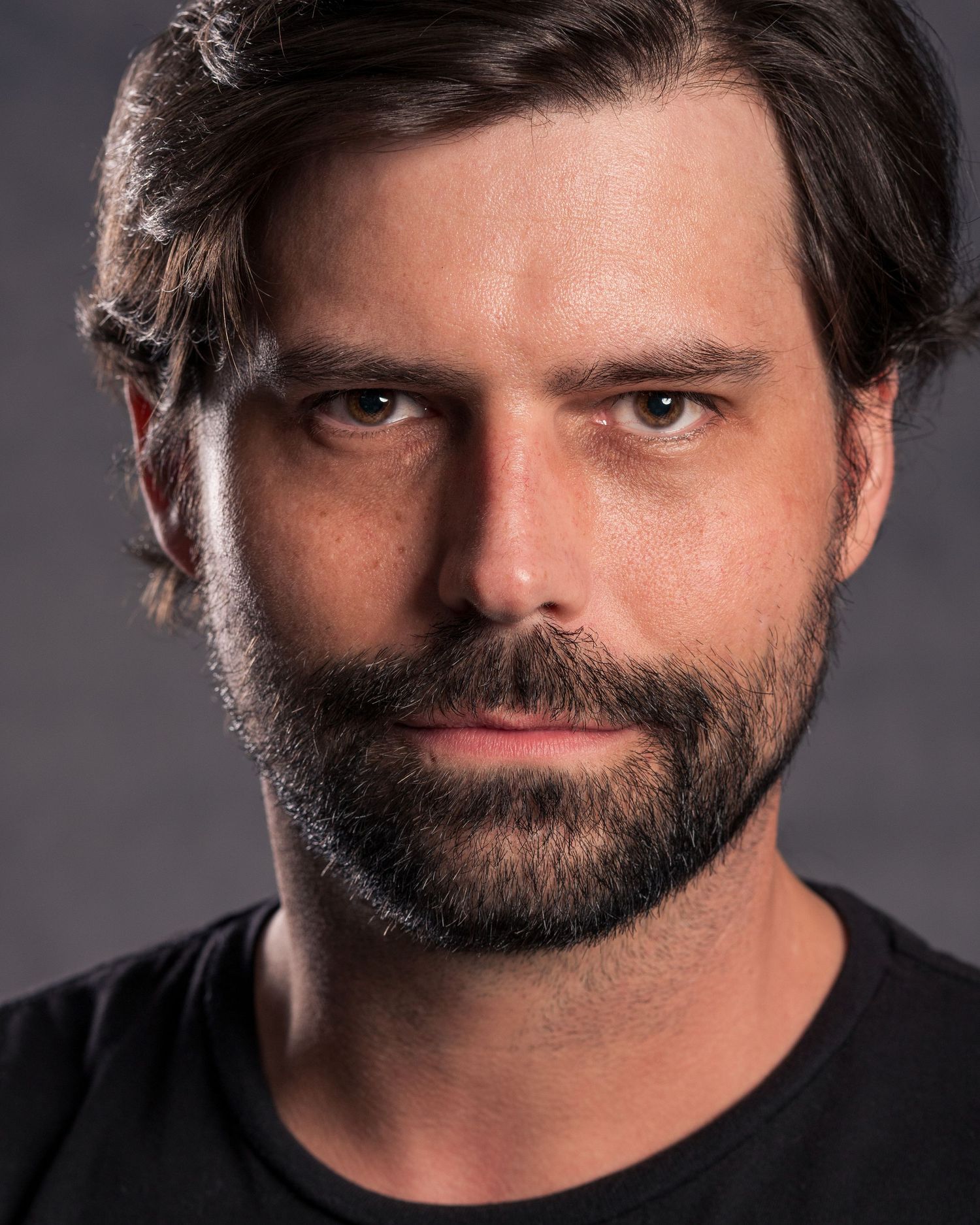 Dramatic portrait of person in gray blazer and black shirt against gray background.
