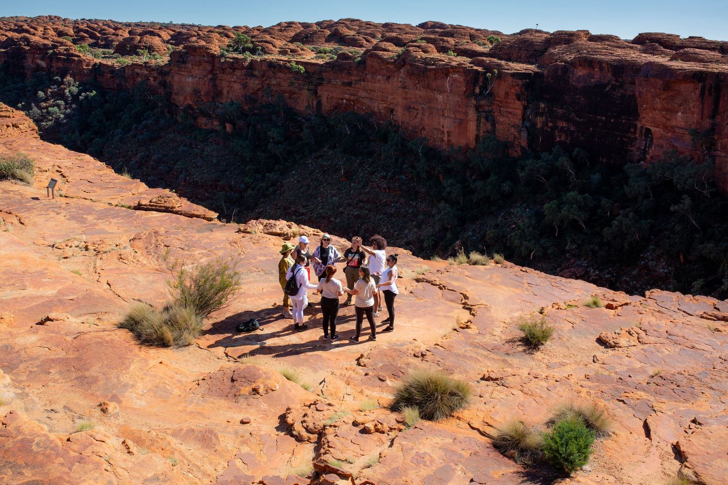 Hikers traverse a winding desert trail through red rock formations in a scenic canyon landscape.
