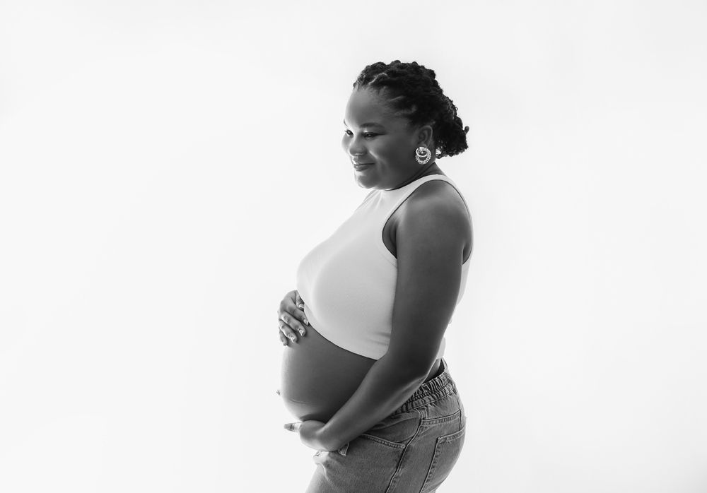 Black and white side view portrait of an expectant mother in a white top holding her pregnant belly. During a London maternity photoshoot