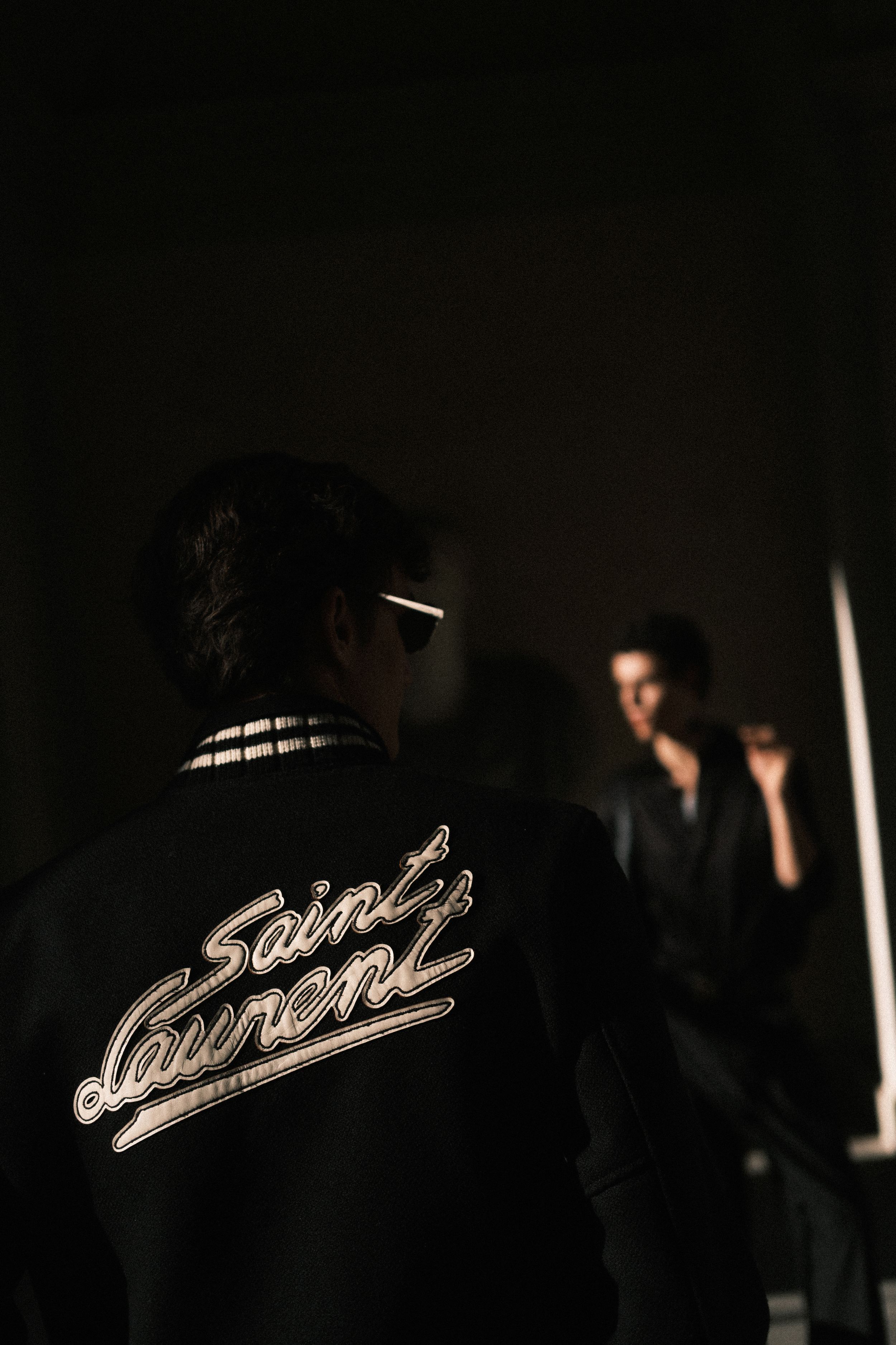 A dark moody photo showing a Saint Laurent logo jacket from behind in low lighting.