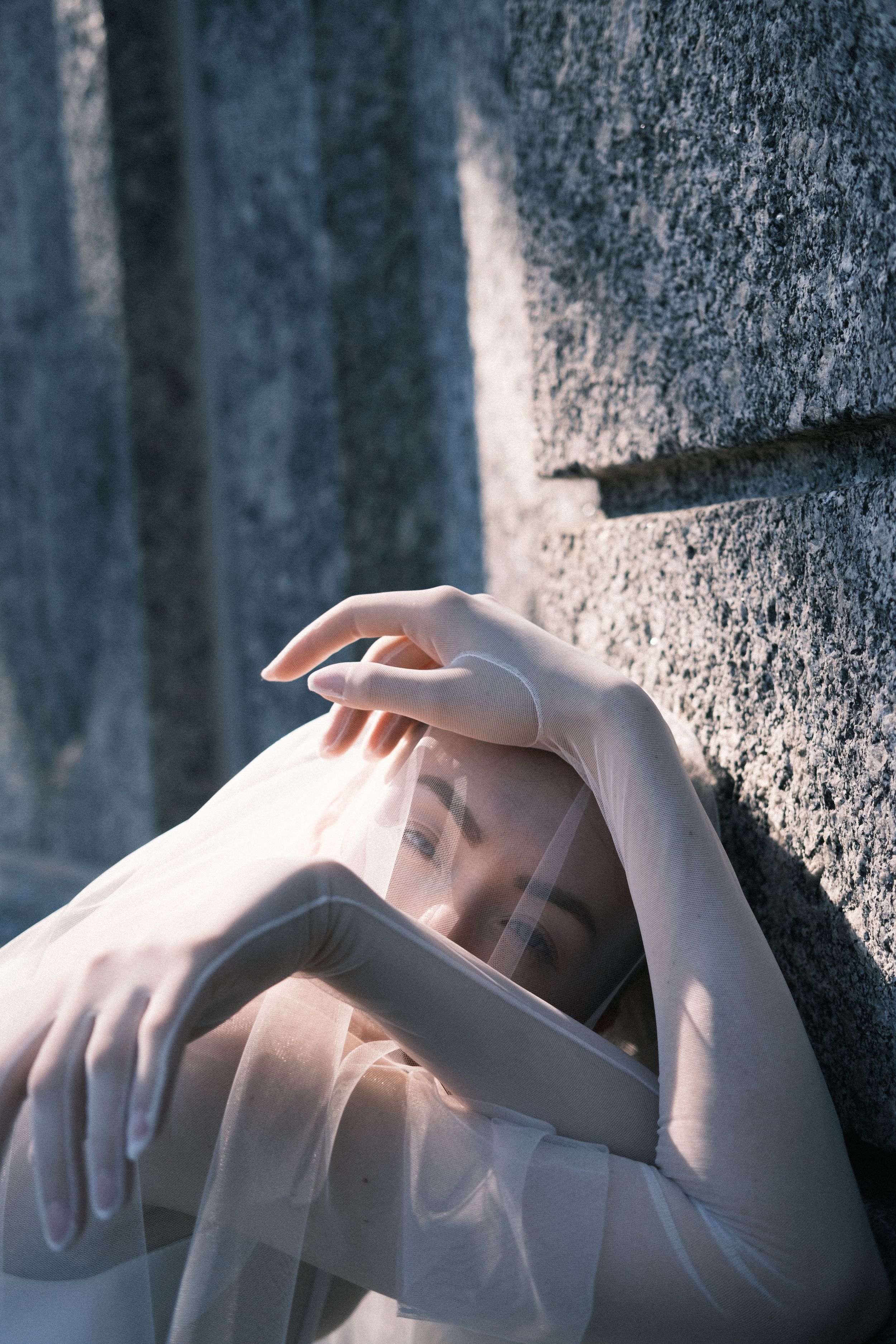 Artistic portrait with soft lighting showing hands against a textured concrete wall.