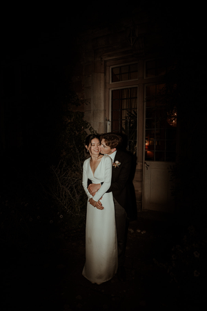 Wedding couple embraces in romantic low-light setting in front of classic doorway with backlit glow at Askham Hall.
