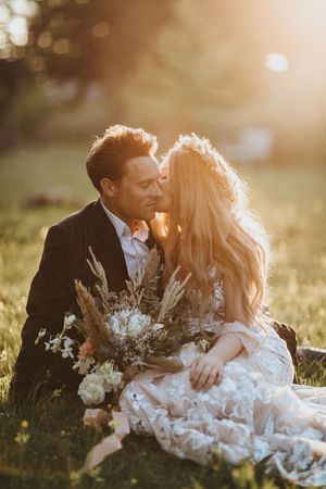 Newlyweds share intimate moments in a sunlit field with white floral arrangements at sunset. Image taken by Lincolnshire photographers.
