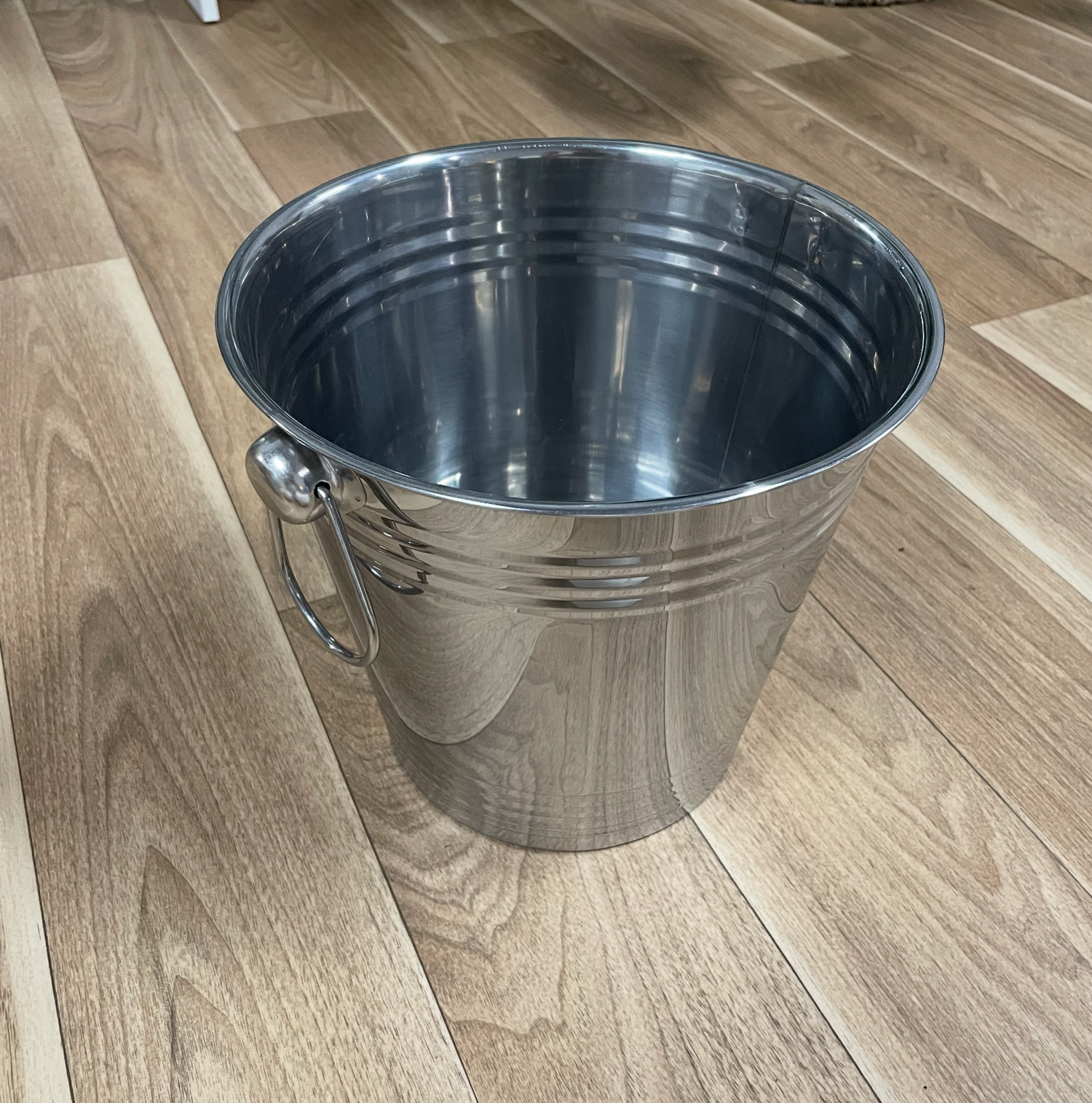 Silver metal bucket with handles photographed at different angles on hardwood floor.