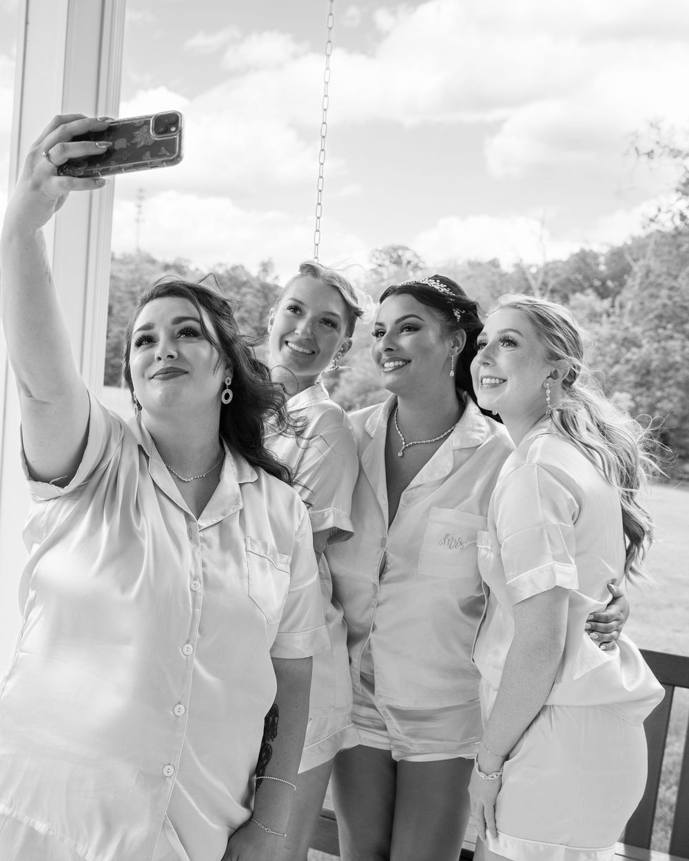 Four friends in white outfits taking a selfie together outdoors in black and white photography.