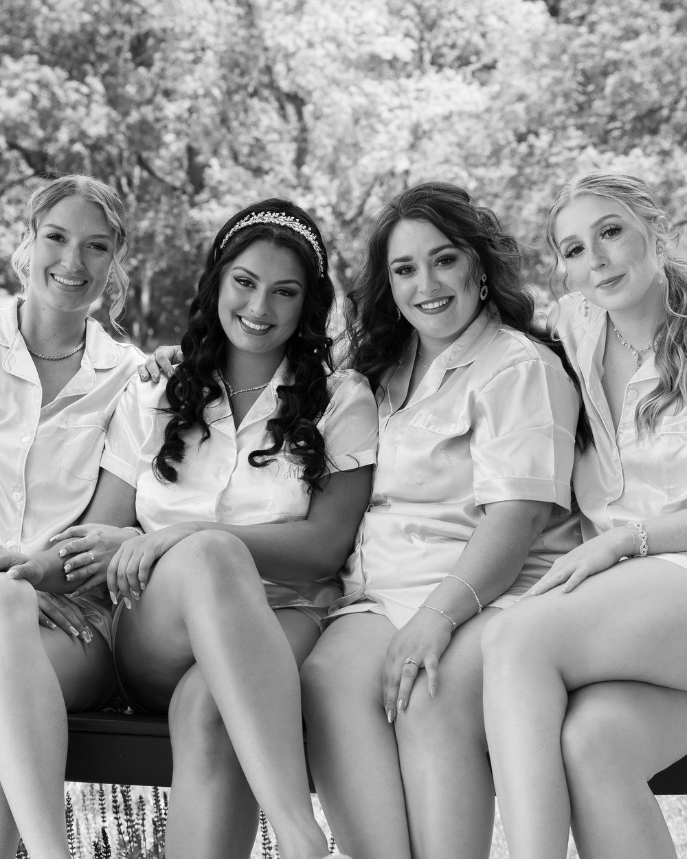 A black and white photograph shows a group of people in white tops sitting together on a bench outdoors.