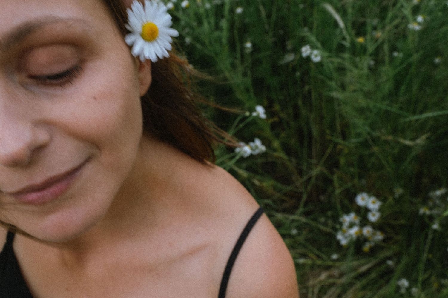 White daisy flower decorates long flowing hair against a natural green background.