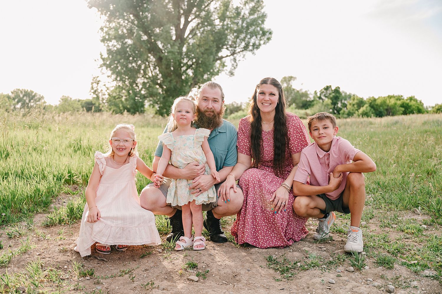 A rustic family photo session in a grassy meadow captured in warm sunlight during golden hour.