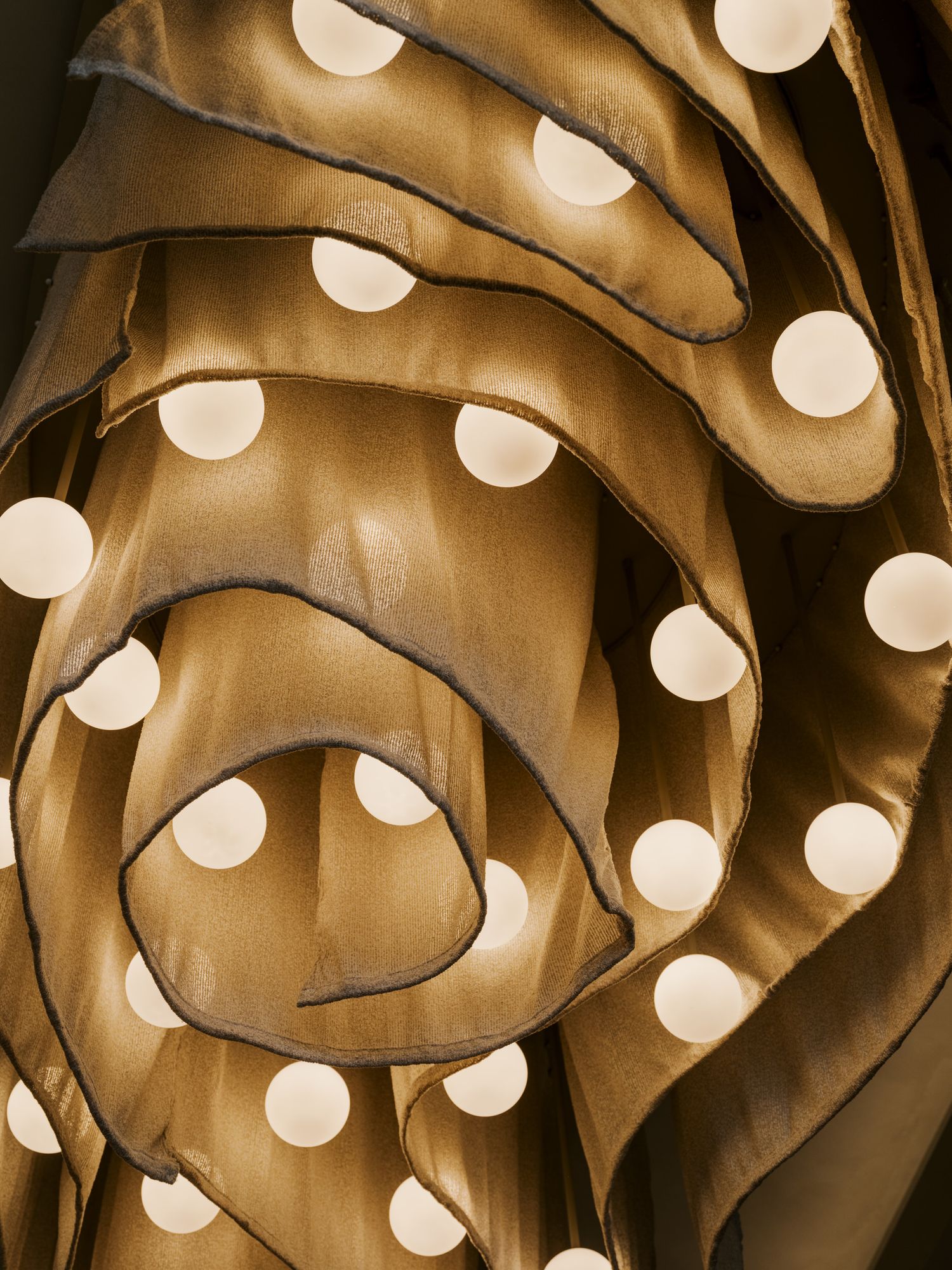 Abstract curved light fixture with glowing orbs creating a warm sepia-toned pattern of illuminated spheres.