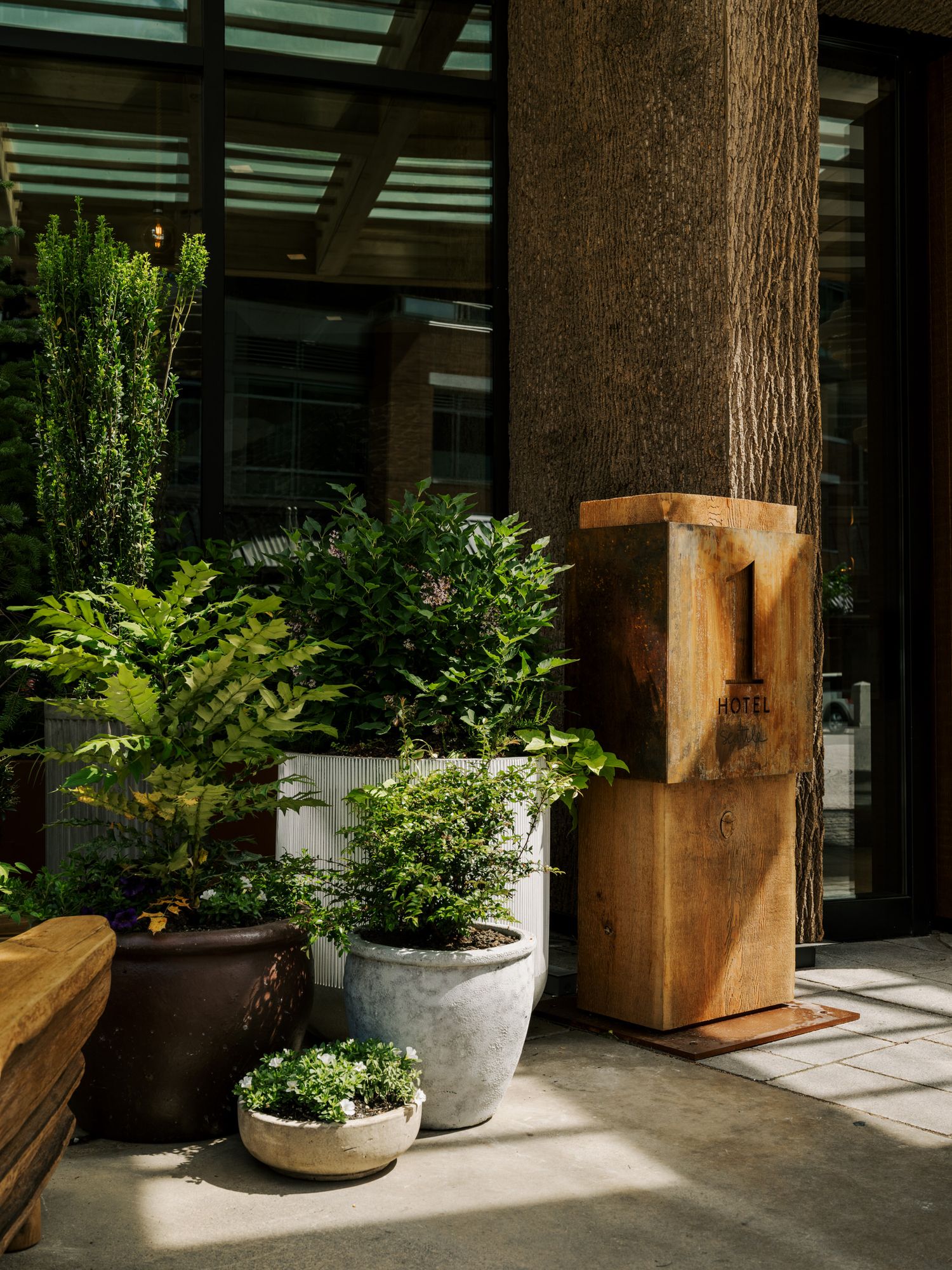 Rustic brown planters of various sizes with lush green plants arranged along a covered outdoor patio space with wooden beams.