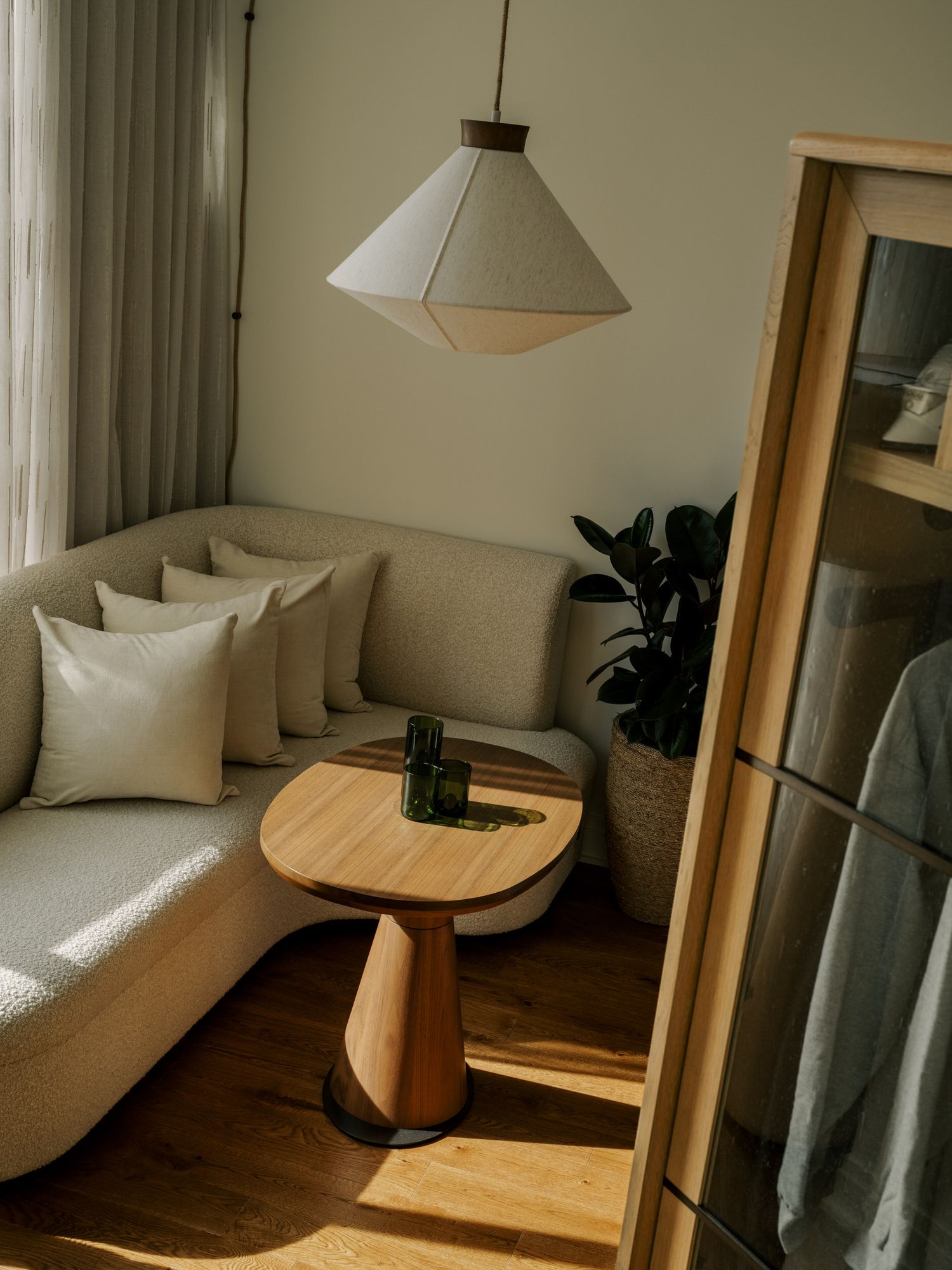 A modern minimalist living room with beige sofa, wooden furniture, pendant lights, and natural sunlight streaming in.