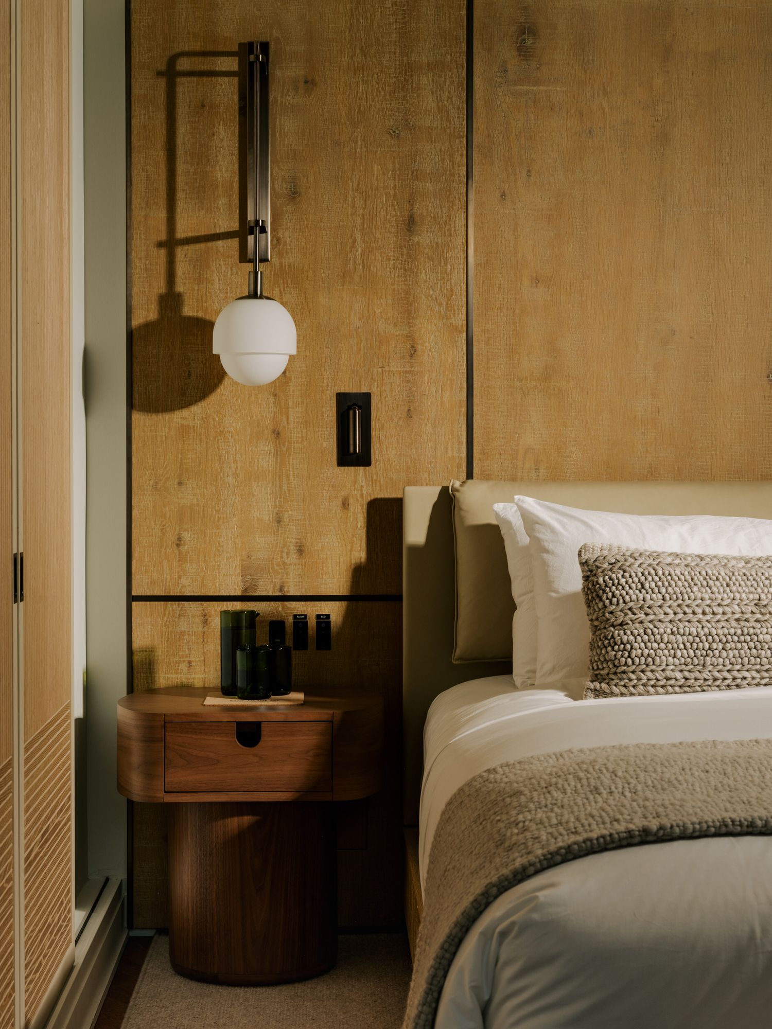 Modern bedroom interior with round globe pendant light, wooden nightstand, and neutral textured bedding.