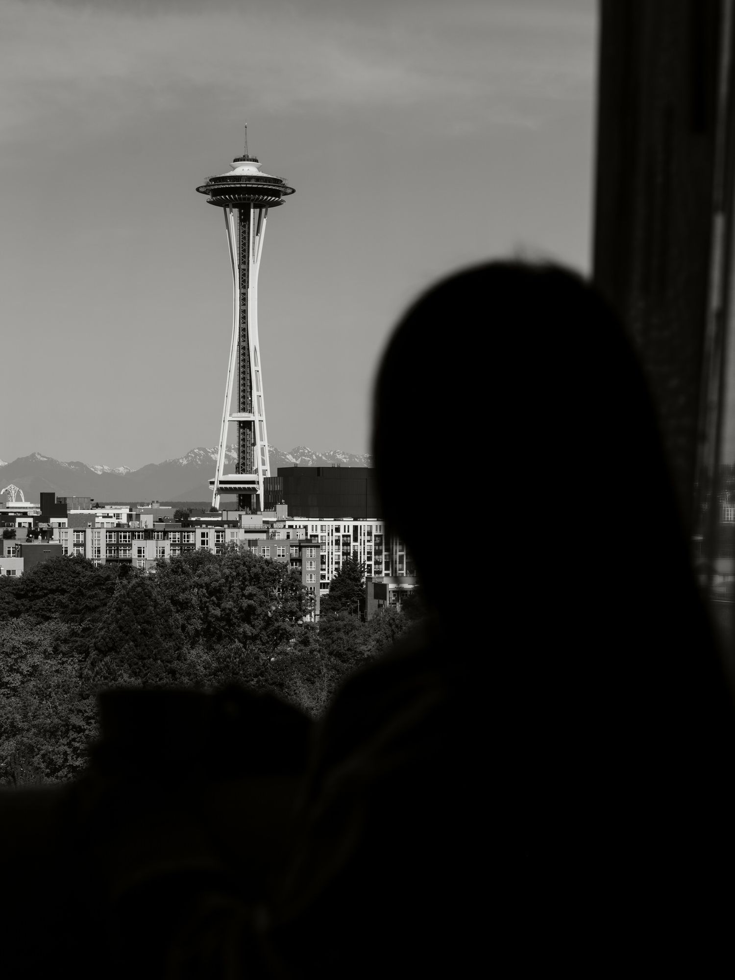 Black and white silhouette of Seattle's Space Needle tower against a cloudy sky with city buildings visible.