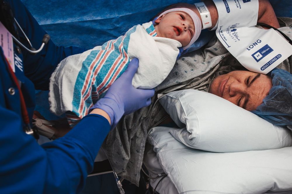 Newborn infant receiving medical attention while lying next to medical equipment on blue bedding.