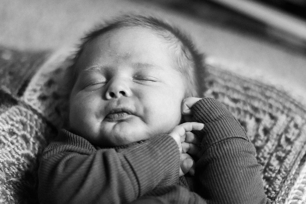 A sleeping baby rests peacefully on a patterned blanket in black and white tones.