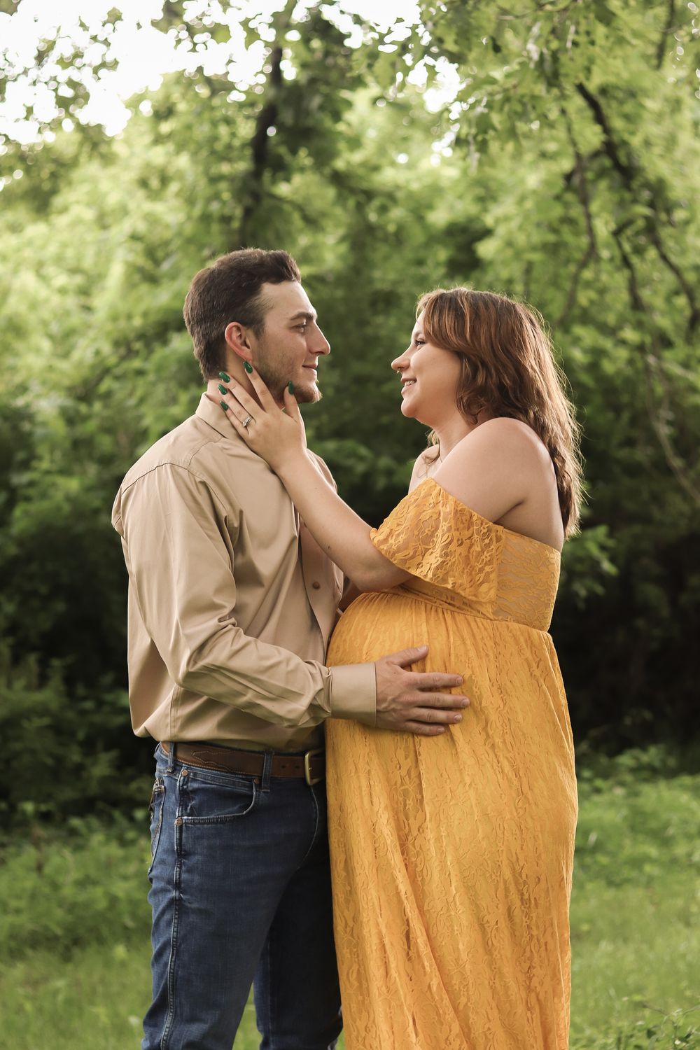 Couple shares intimate moment outdoors with mother-to-be wearing flowing yellow dress during maternity photoshoot.