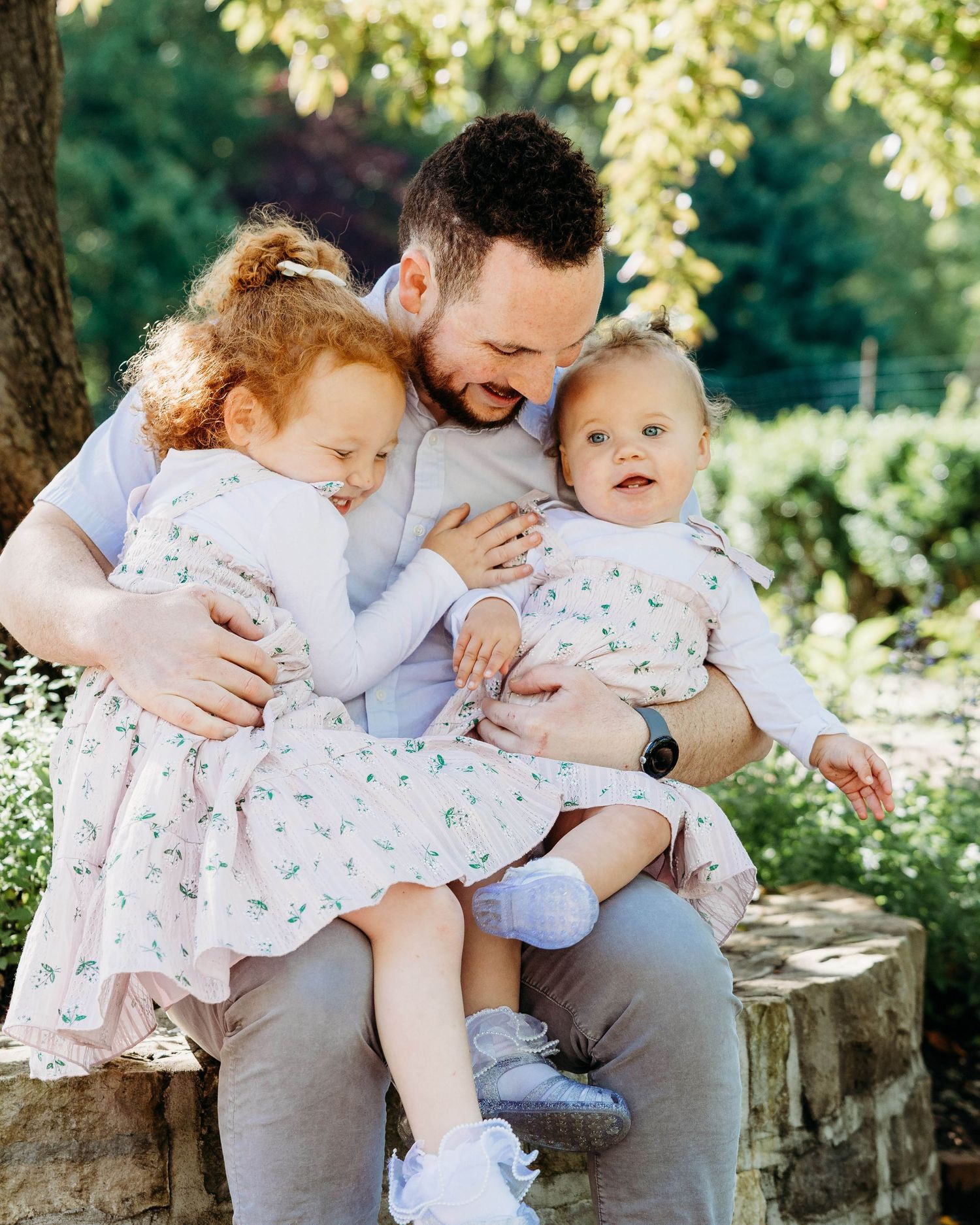 A joyful outdoor family moment captured in soft sunlight as they share tender embraces while sitting on a tree stump.