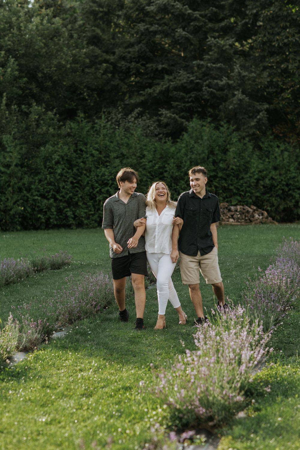 Three friends walking together on a lush green lawn with blooming lavender flowers in the foreground on a summer day.