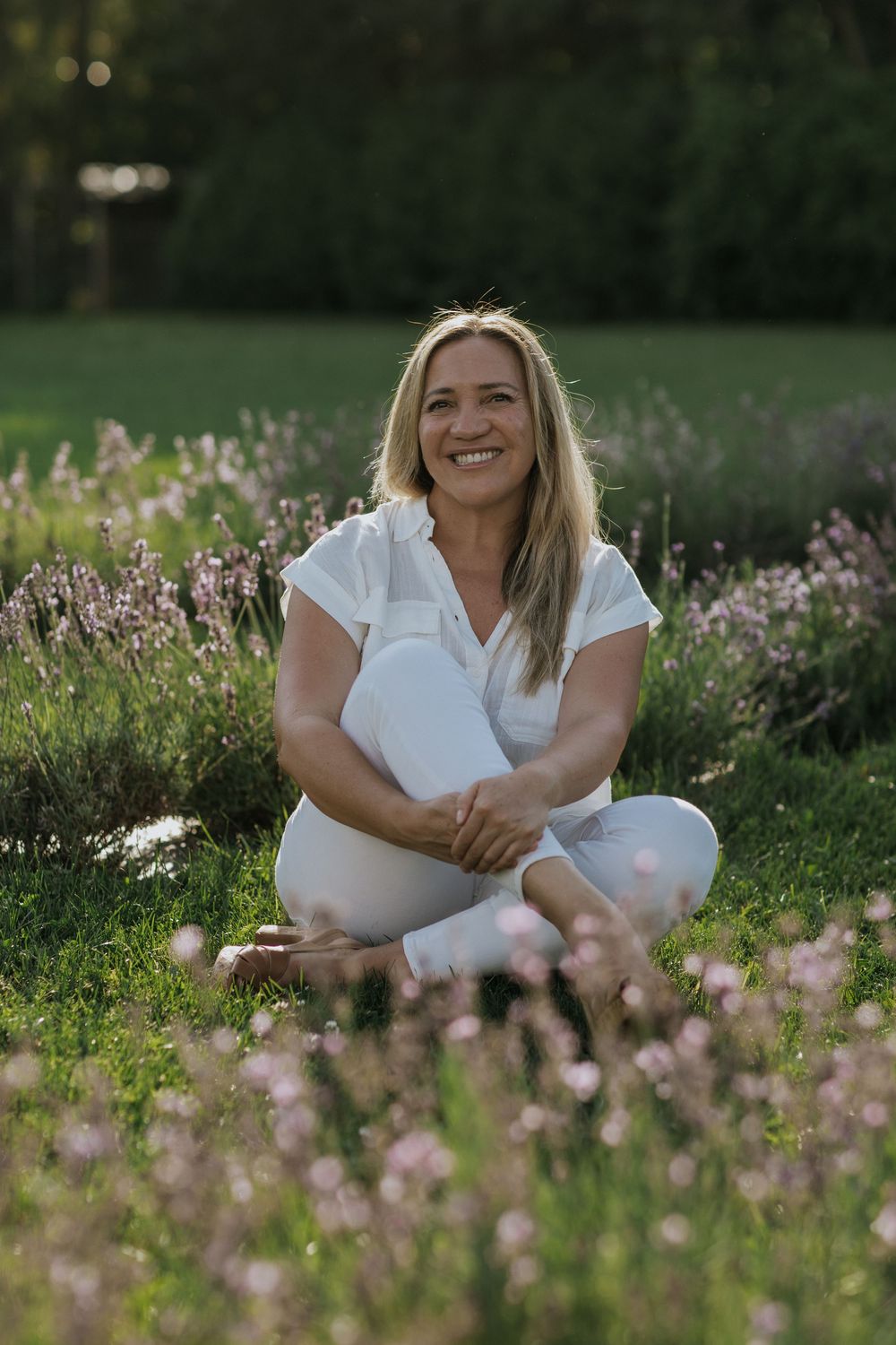 Woman in white sitting cross-legged in a blooming lavender field at sunset.