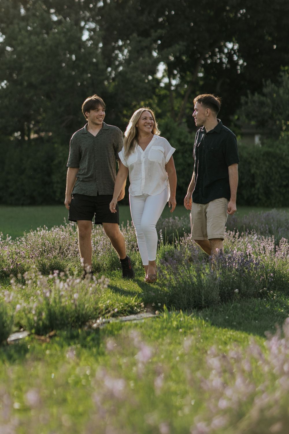 Three friends walking together and laughing in a garden with blooming lavender at sunset.