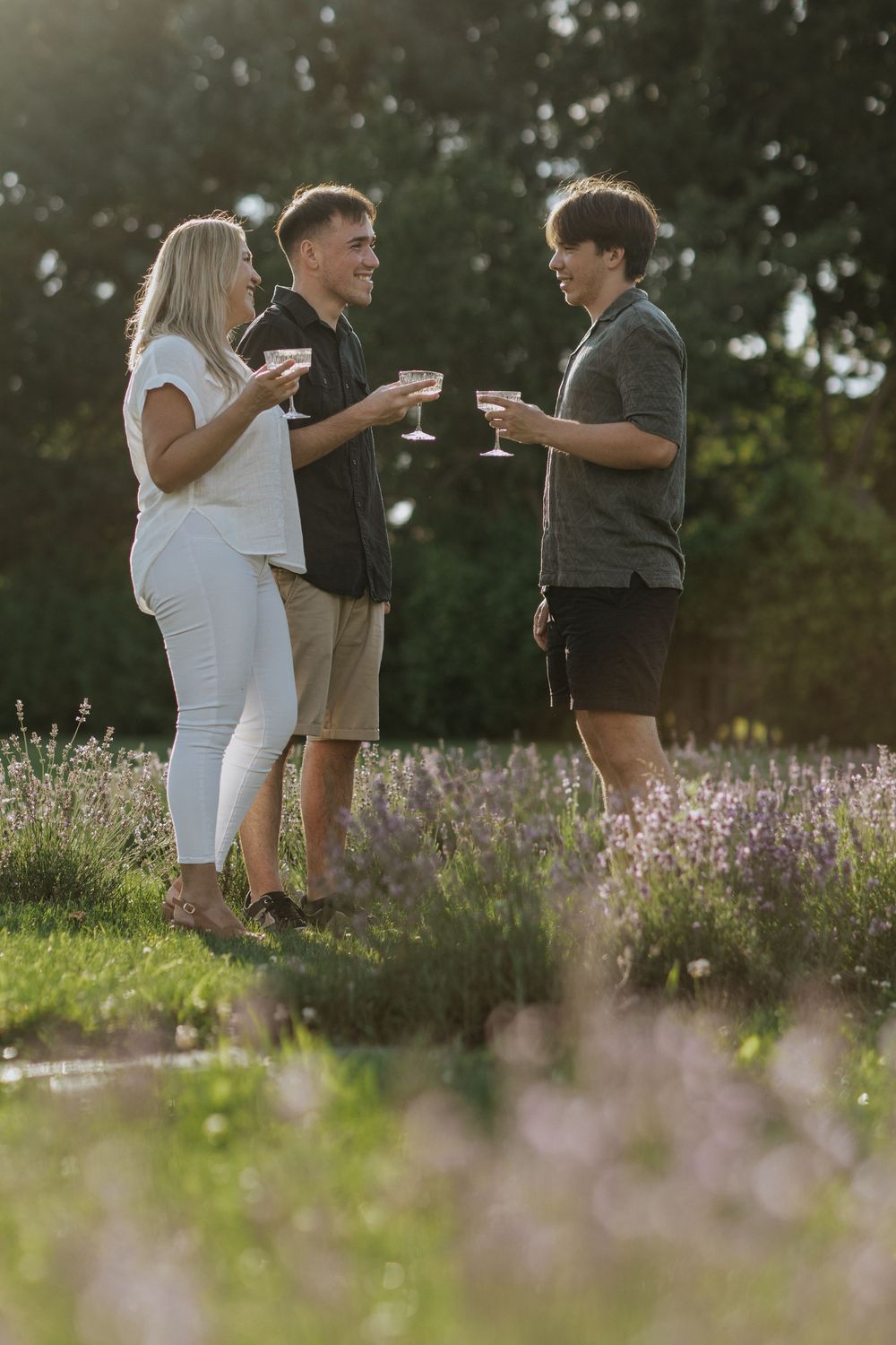 Friends enjoying wine and conversation in a garden surrounded by purple wildflowers at golden hour.