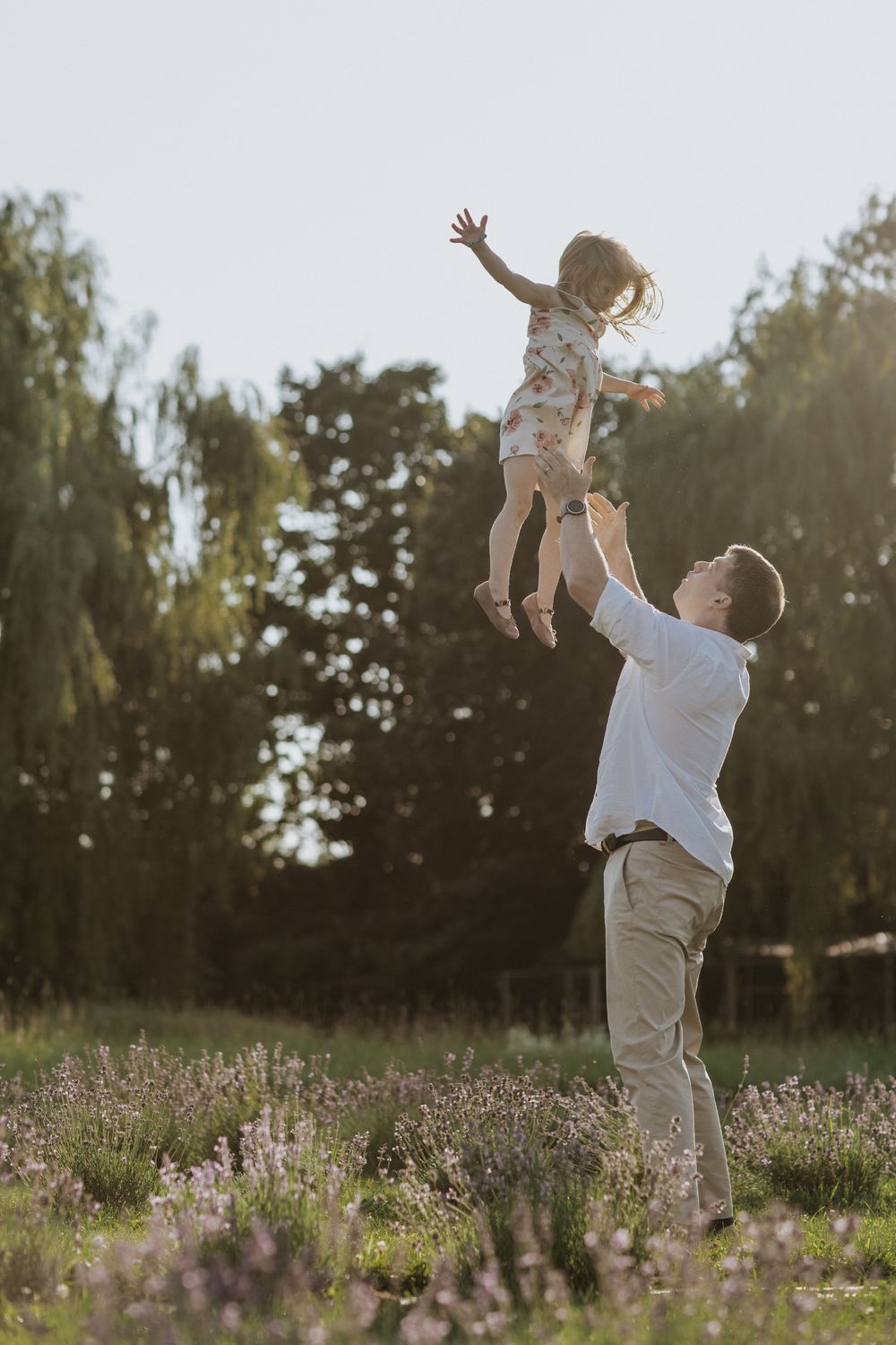 Father playfully lifting child high in the air among wildflowers at sunset.