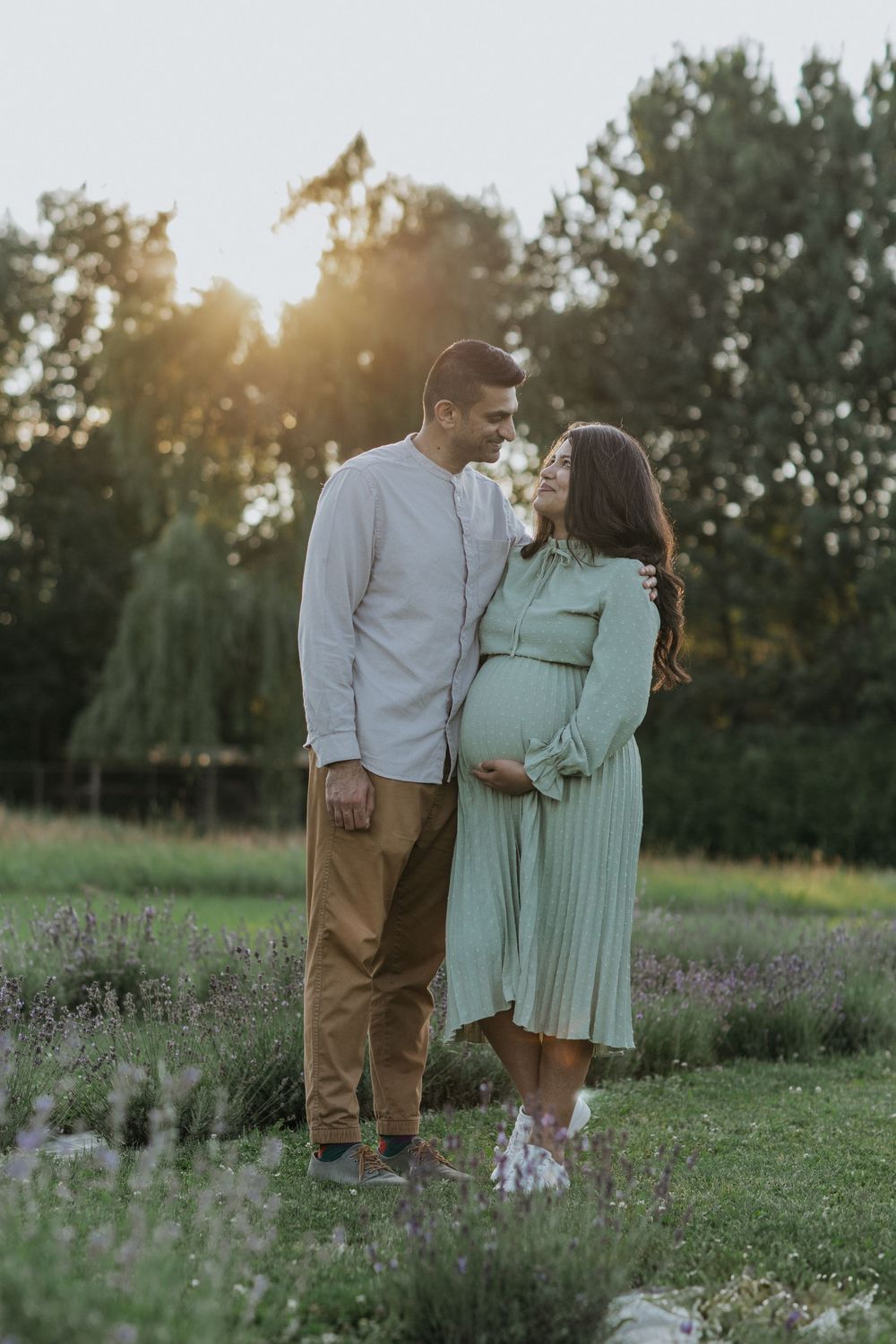 Expecting couple shares an intimate moment in a field of lavender during sunset.