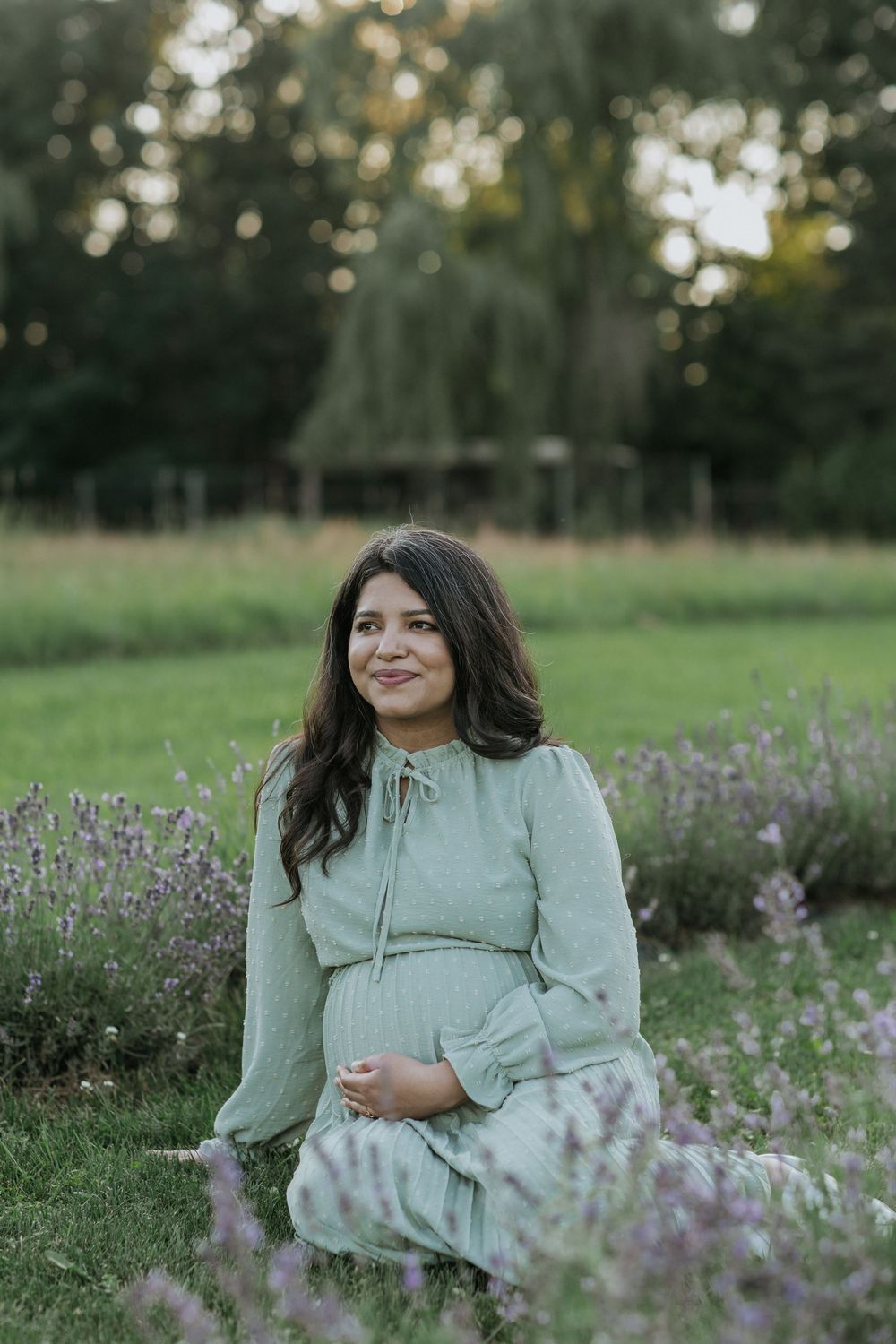 A pregnant mother in a sage green dress poses in a lavender field near Ottawa, ON.