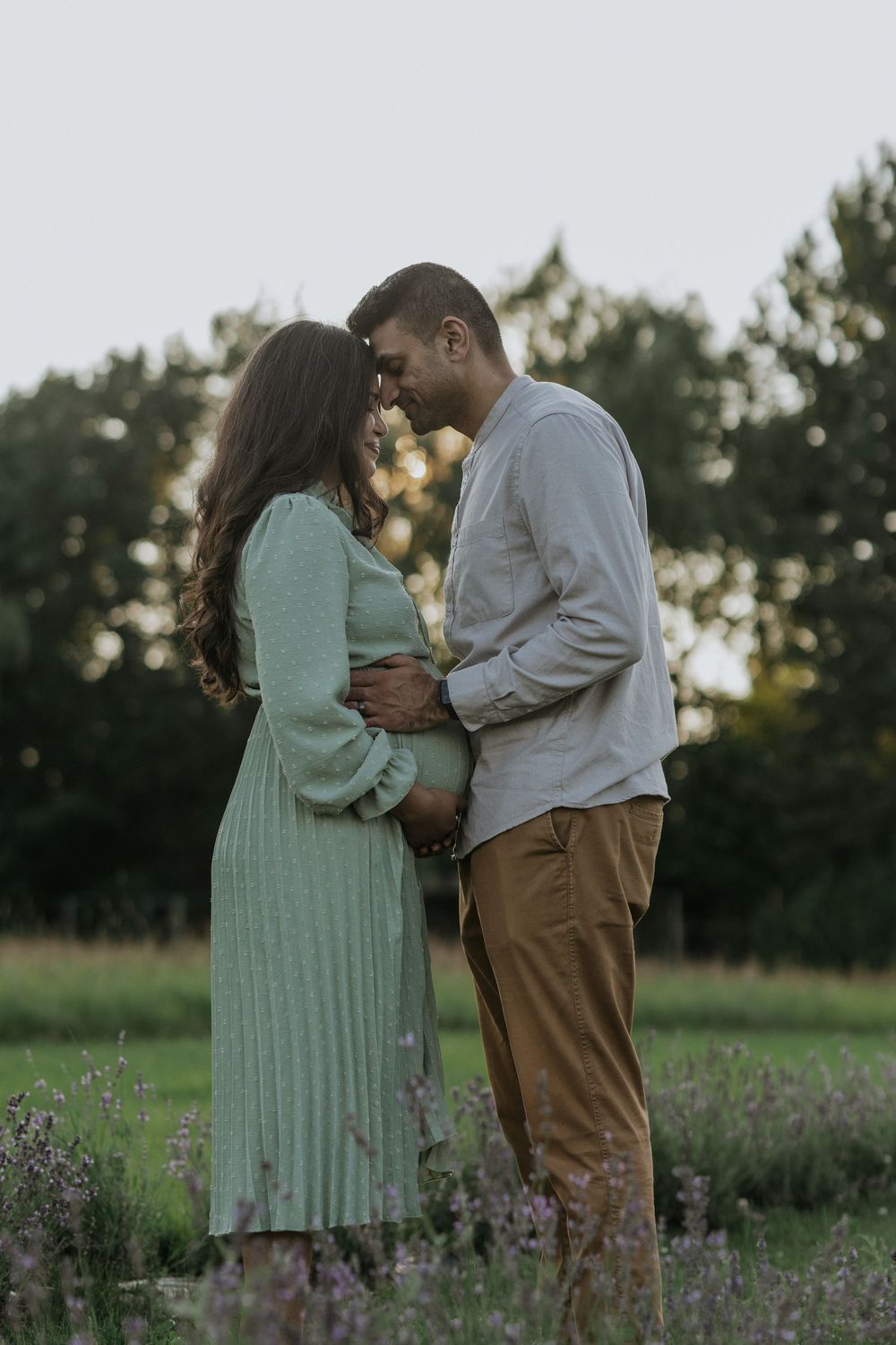 Expectant couple embracing tenderly in a lavender field during golden hour.