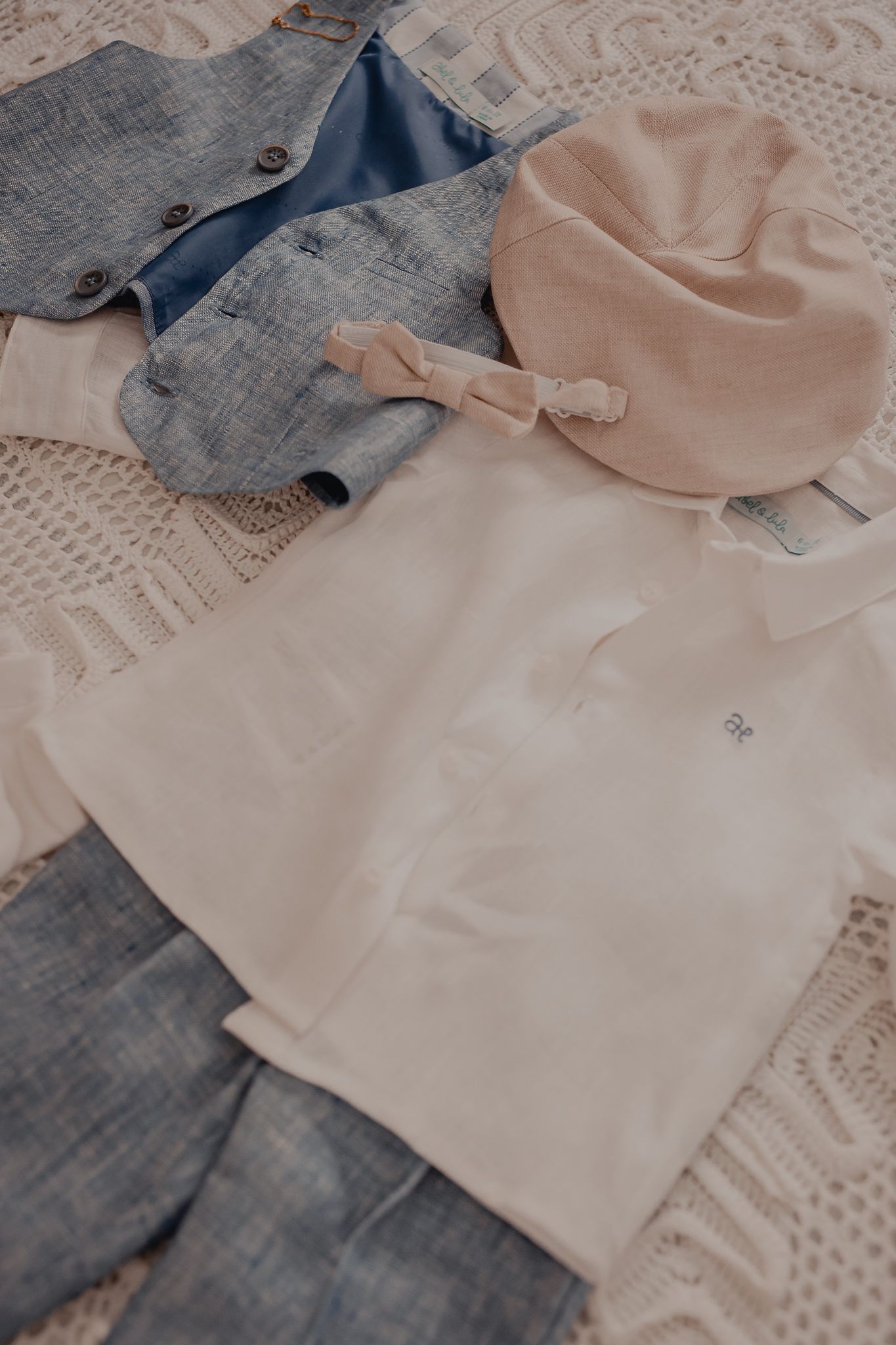 Flat lay of light colored clothing items including denim and beige garments on textured fabric.