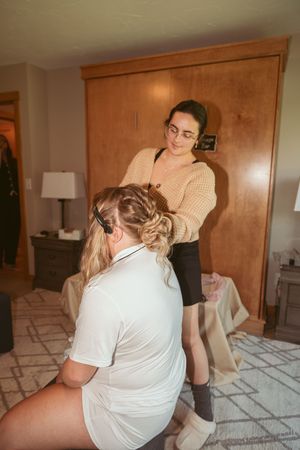 Hair stylist in beige sweater working on an updo hairstyle in a cozy interior setting.