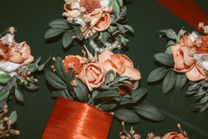 Peach-colored roses and greenery arranged in a copper-colored vase against a dark background.