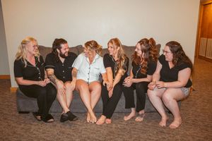 Wedding party members relaxing together in informal poses on carpeted floor.