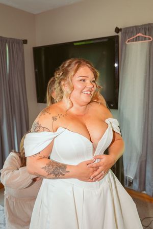 Woman in white dress getting ready with assistance during a wedding preparation moment.